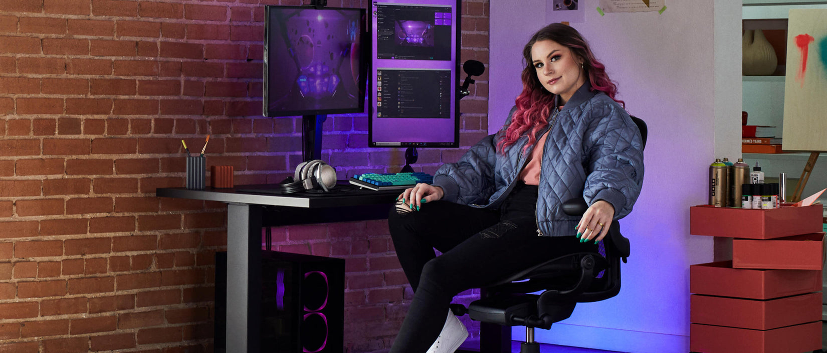 Photo of gamer Electra facing camera sat on Aeron gaming onyx black in front of Nevi gaming desk in black with Ollin monitor