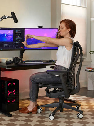 Photo of Dr Lindsey Migliore sat in a Embody gaming chair doing wrist flexion stretches in Embody gaming chair in cyan with Nevi gaming desk