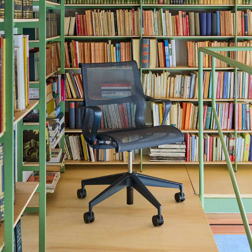 A nightfall navy blue Herman Miller Setu ergonomic reading chair in a colourful home library.