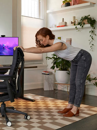 Photo of Dr Lindsey Migliore leaning on the back of the Embody gaming chair doing back, shoulder and leg stretches