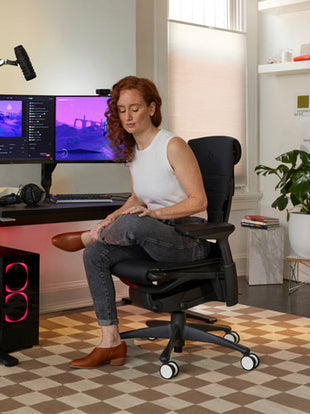 Photo of Dr Lindsey Migliore sat with one left ankle resting on right knee doing a hip and buttock stretch in Embody cyan gaming chair