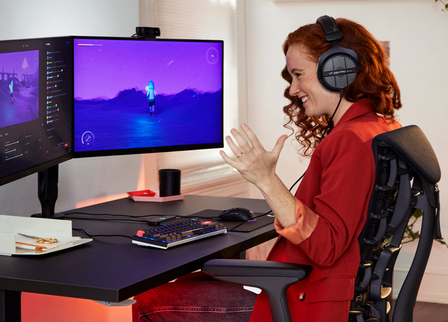 Photo of Dr Lindsey Migliore smiling playing computor game in Embody cyan gaming chair with Nevi gaming desk in black
