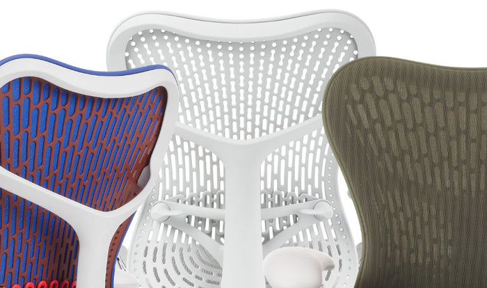 Close-up of three Mirra 2 office chairs by Herman Miller, showing the range of colours available. The first is blue, orange and white, the second is white only and the third is green.