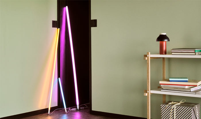 Three HAY neon LED tubes in three sizes and an array of colours, leaned against a white wall.