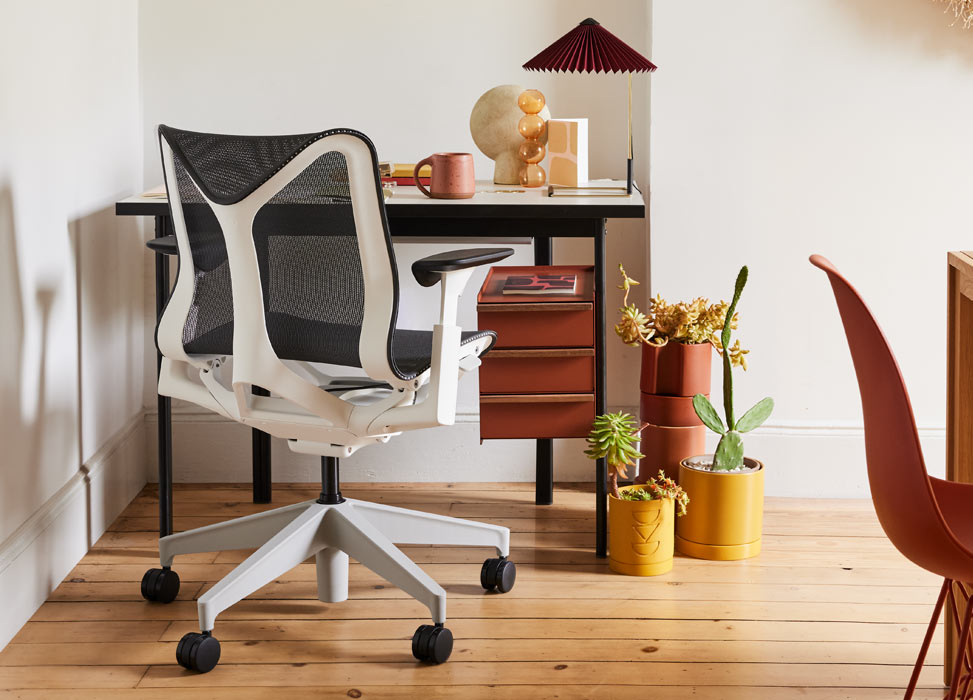 A blue and white Cosm office chair by Herman Miller, positioned in front of a black and terracotta Mode desk by Herman Miller. Set in a home office with wooden floors and white walls, accessorised with a Matin table lamp and indoor plants.