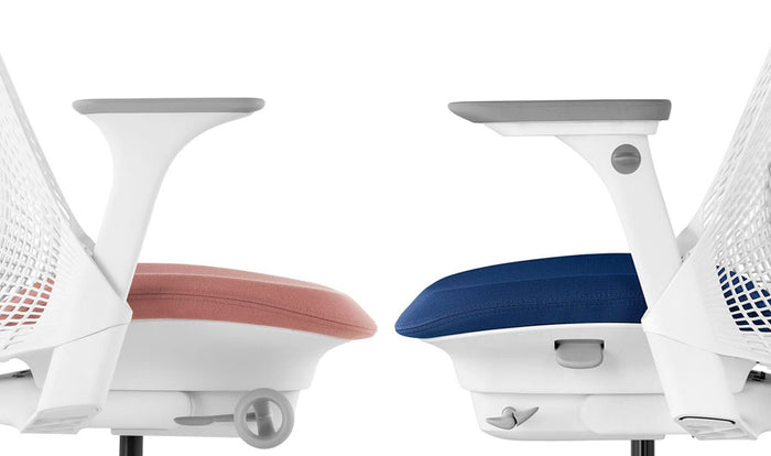 Side view of two Herman Miller Sayl office chairs facing each other. The left chair shows the fixed armrest and the right chair shows the fully adjustable armrest.