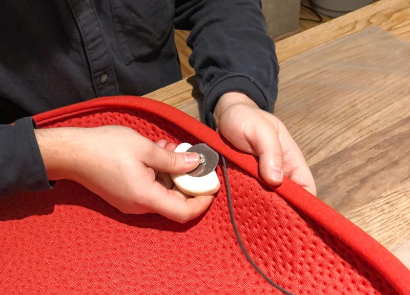 A person producing a red fabric seat pad for a Herman Miller Zeph office chair.