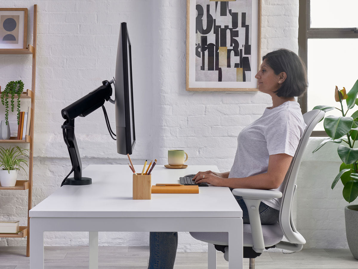 Lady sat at desk in Lino office chair in mineral white with grey seat showing wrist level on desk as part fo sitting properly