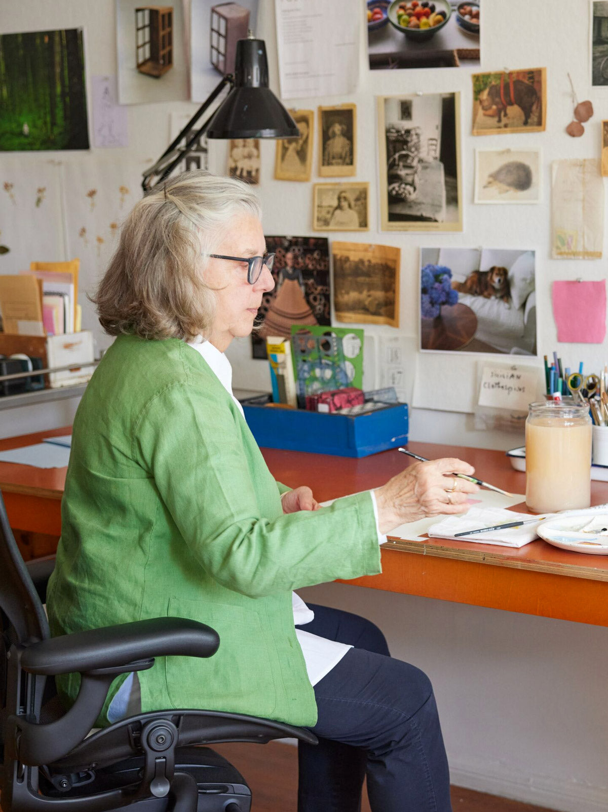 Photo of illustrator, painter and author sitting at desk painting in an Aerong office chair in graphite