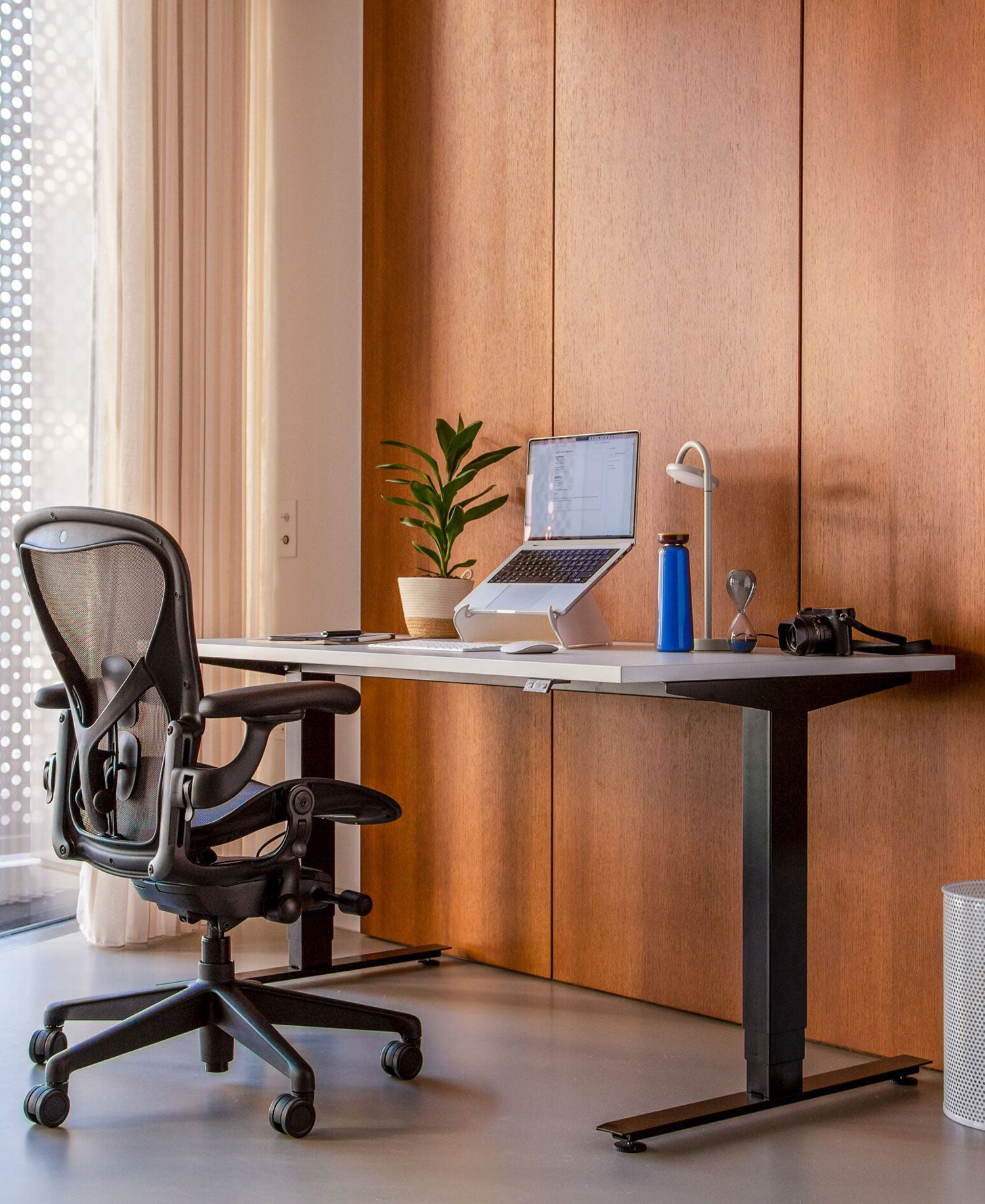 Home office with Aeron office chair in graphite in front of Nevi sit-stand desk with black legs and white top and oripura laptop stand.