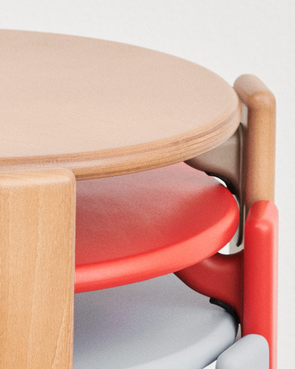 Close-up of three Rey chairs by HAY, in beech, red and blue, stacked on top of one another.