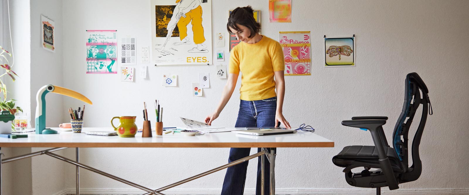 Illustrator, painter and author Molly Rose Dyson stood at her studio workspace with an Embody gaming chair in black and cyan blue