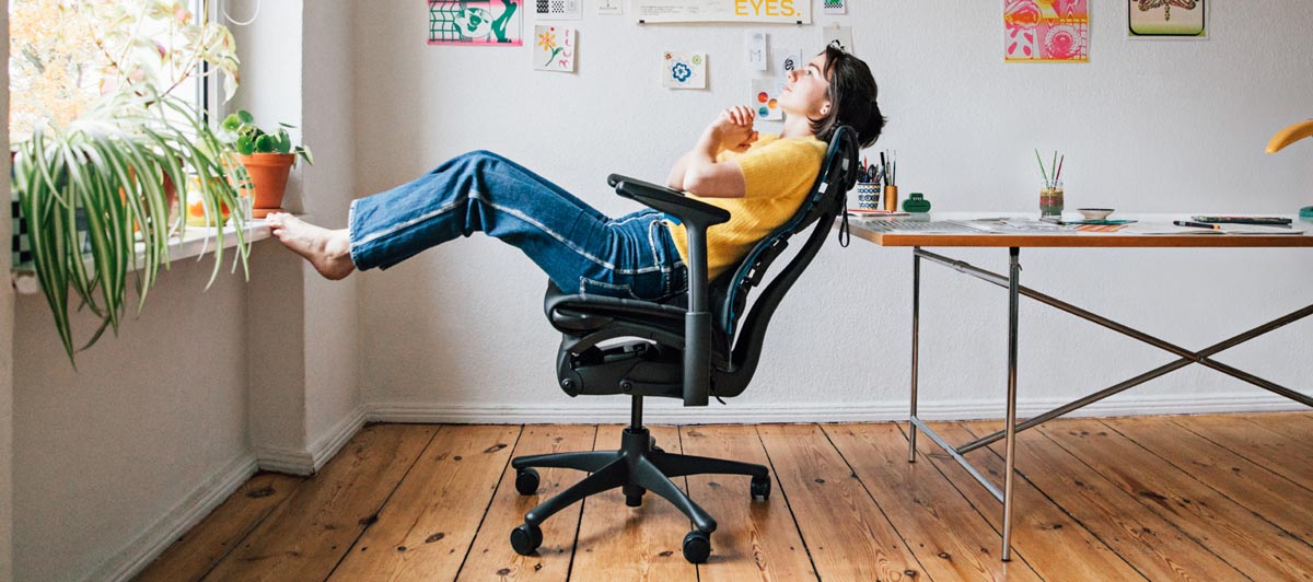 Illustrator, painter and author Molly Rose Dyson in her studio workspace sat reclining in an Embody gaming chair in black and cyan blue