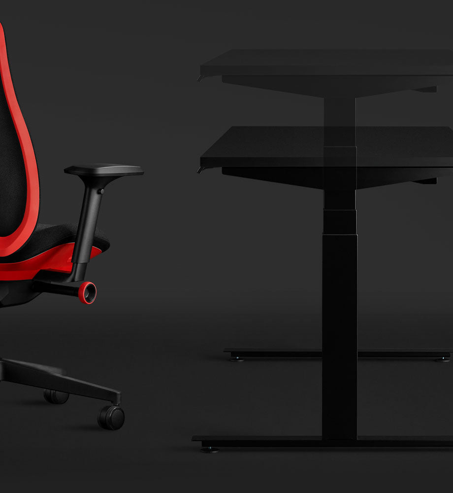Side view of a black Nevi gaming desk and red Vantum gaming chair by Herman Miller, highlighting the sit-stand element of the desk.