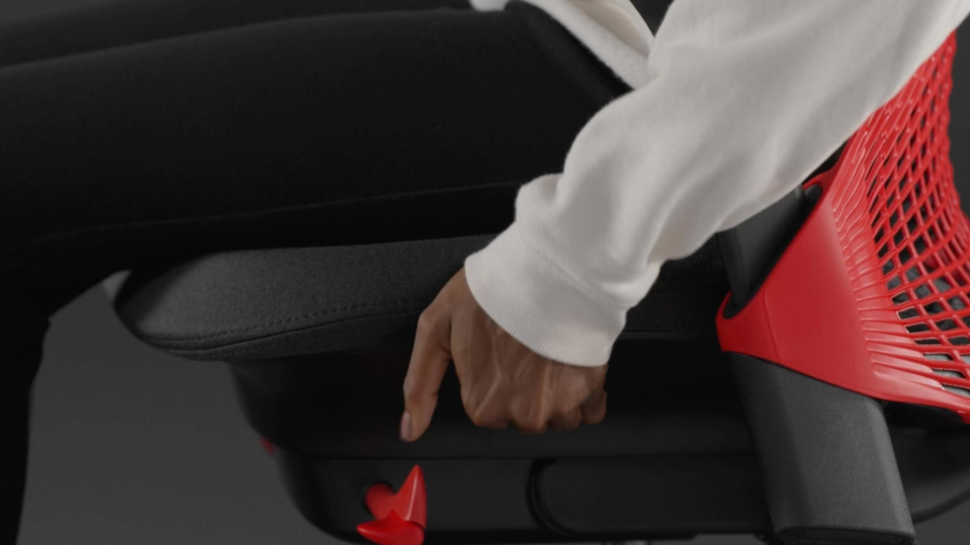 A video of a person sitting in a red and black Sayl gaming chair by Herman Miller, reaching beside the chair to adjust the seat depth.
