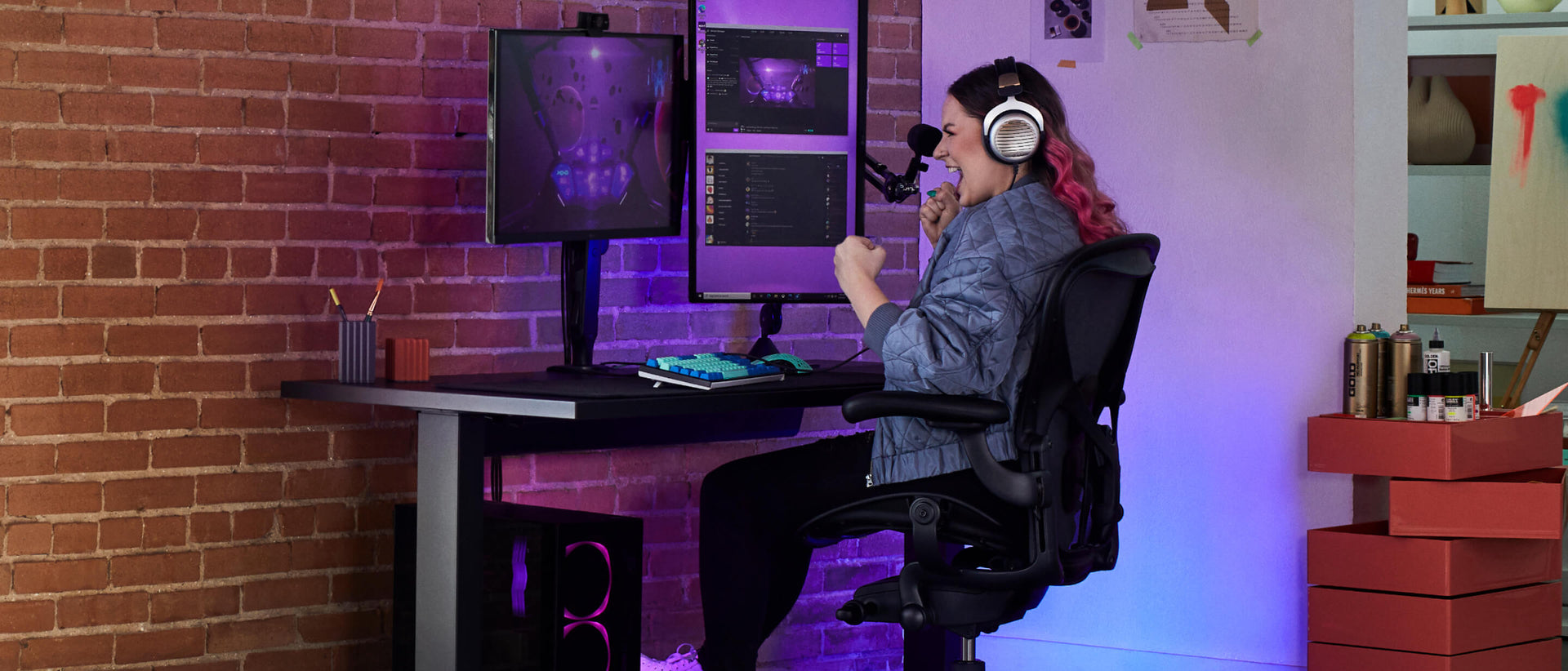 Electra smiling with clenched fists whilst gaming sat on Aeron gaming onyx black with Nevi gaming desk in black and Ollin monitor arm