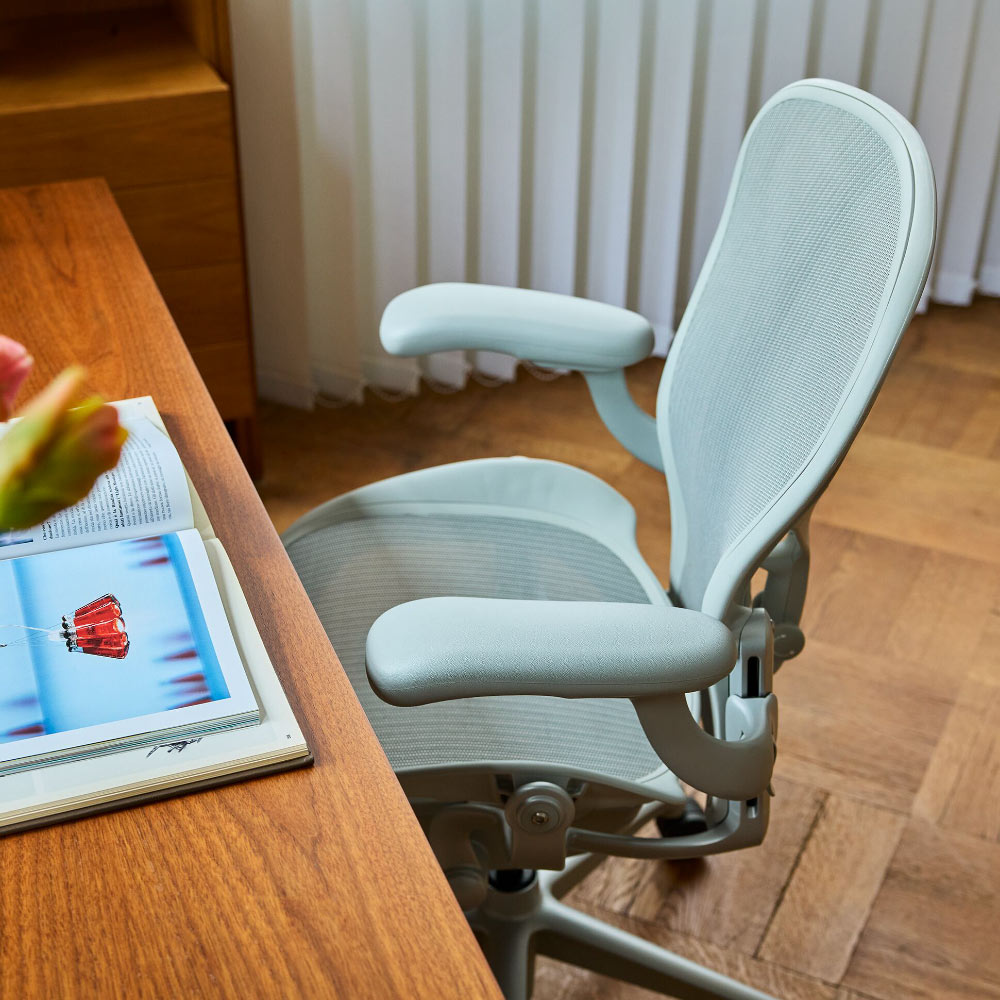 Close view of a pale grey mineral Herman Miller Aeron ergonomic desk chair at a wooden table.