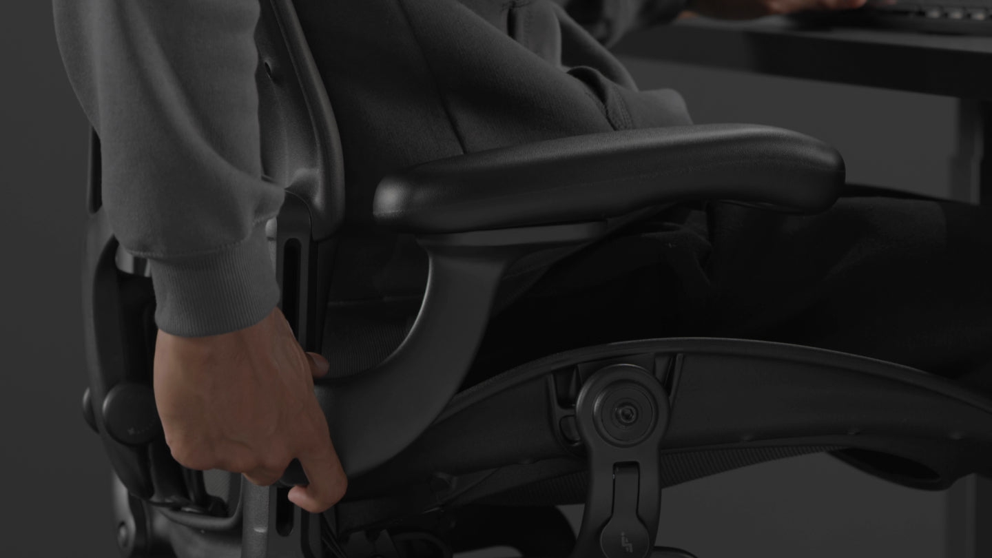 A video of a person sitting in a black Aeron gaming chair by Herman Miller, reaching beside the chair to adjust the arms.