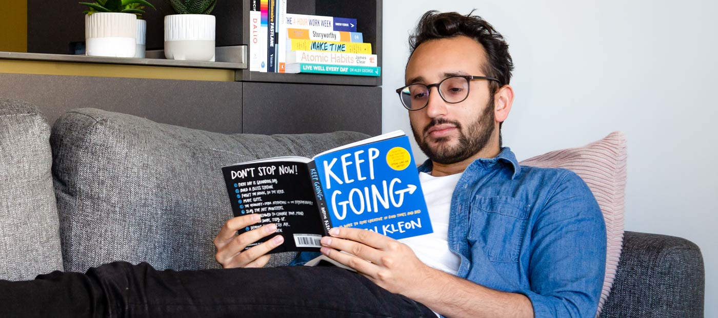 Photo of Ali Abdaal laying on sofa reading a book called Keep Going