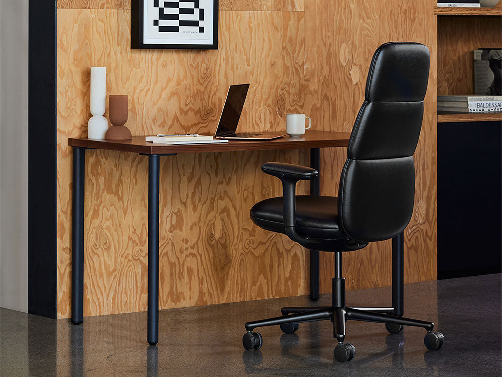 A black Asari office chair is positioned in front of a black and walnut OE1 desk in an indoor setting with a mid-century modern interior design aesthetic.