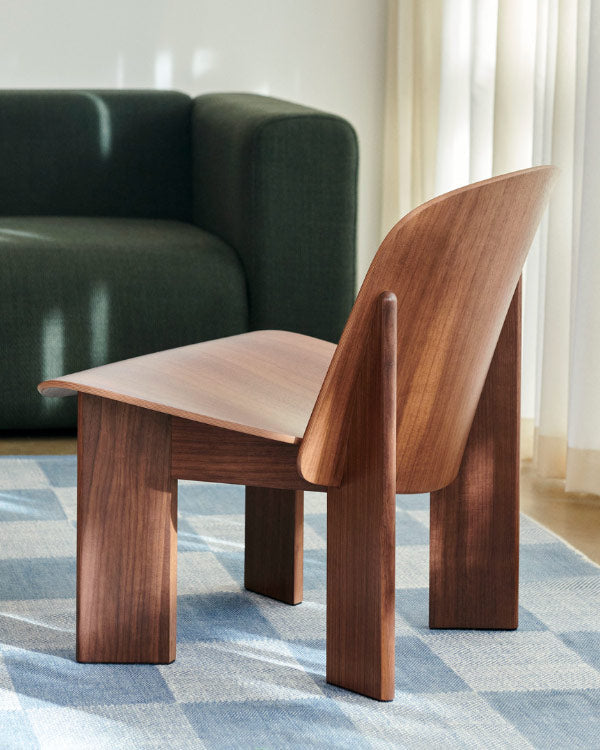 Rear view of a walnut Chisel lounge chair by HAY, set in an indoor home space on a blue checkered rug.