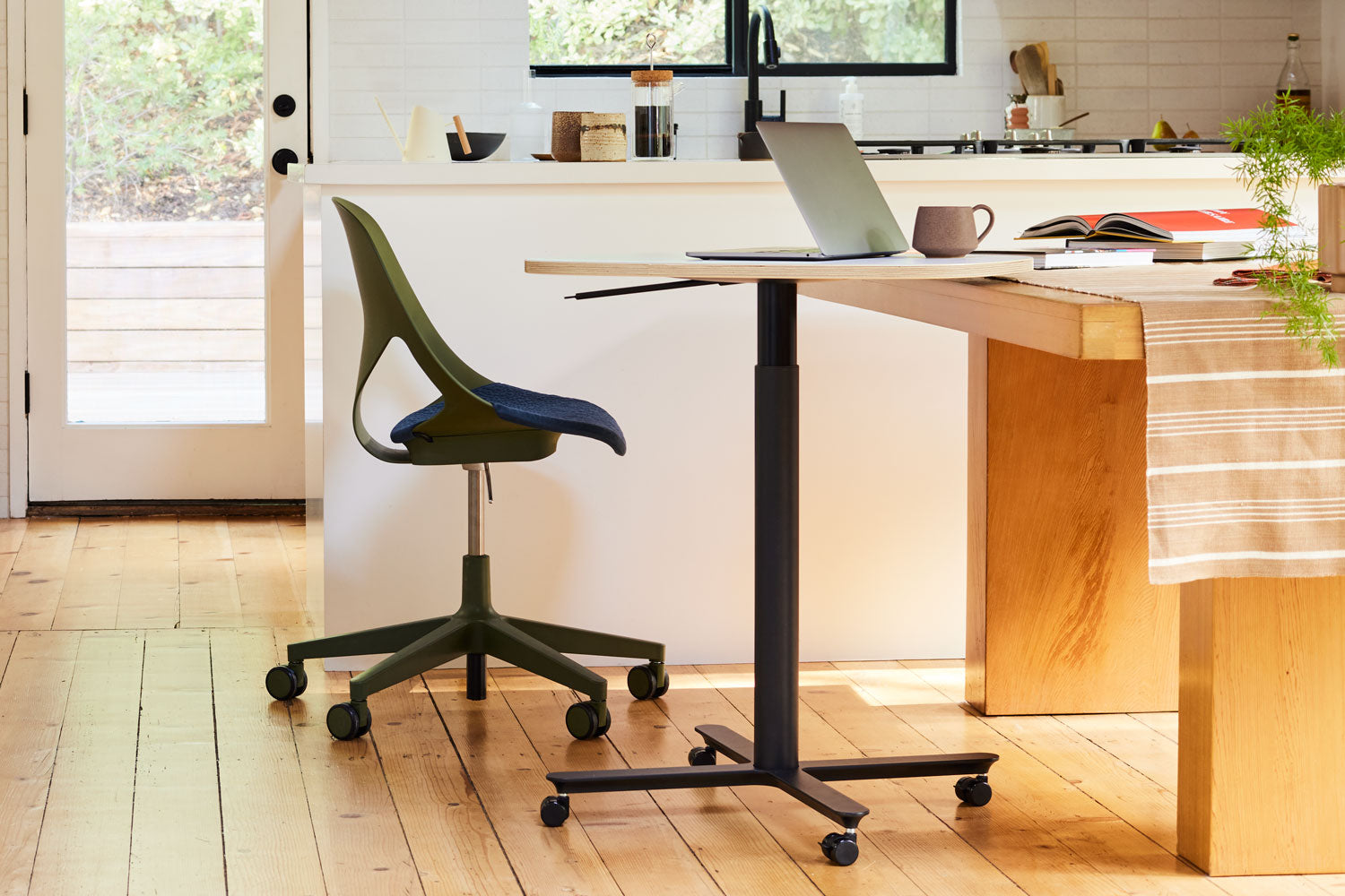 Photo set in a home kitchen with Zeph office chair in olive with midnight blue seat pad along with compact hieght adjustable Passport work table