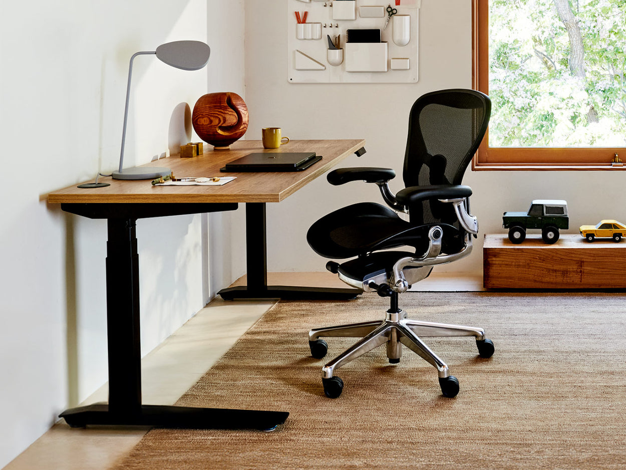 A bright home office featuring a Herman Miller Aeron ergonomic office chair in black and chrome alongside an oak-topped Jarvis sit-stand desk.