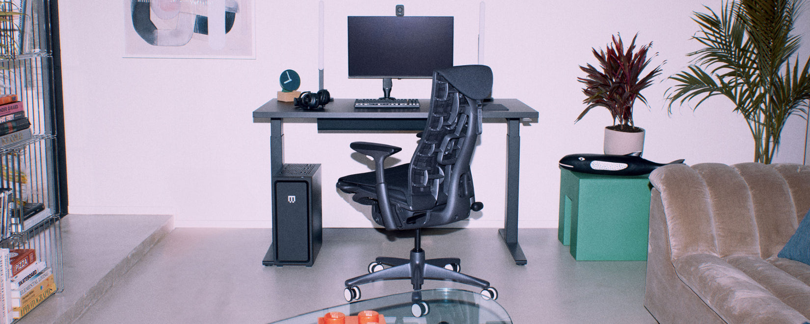 An ergonomic PC gaming setup featuring a black Herman Miller Embody gaming chair and Nevi sit-stand gaming desk in a white modern living room.