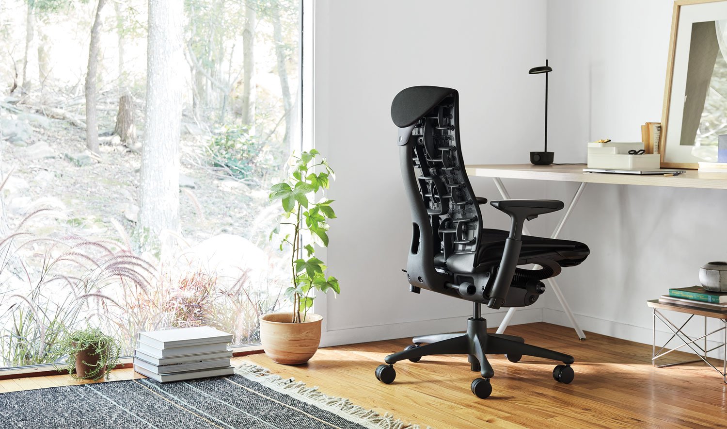 A black Embody office chair by Herman Miller, situated in an indoor environment. The space incorporates elements such as furniture, flooring, and decorative items like a flowerpot and vase.