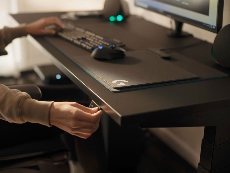 A video of a person sitting at a black Nevi gaming desk by Herman Miller, pressing a button to lower the desktop.