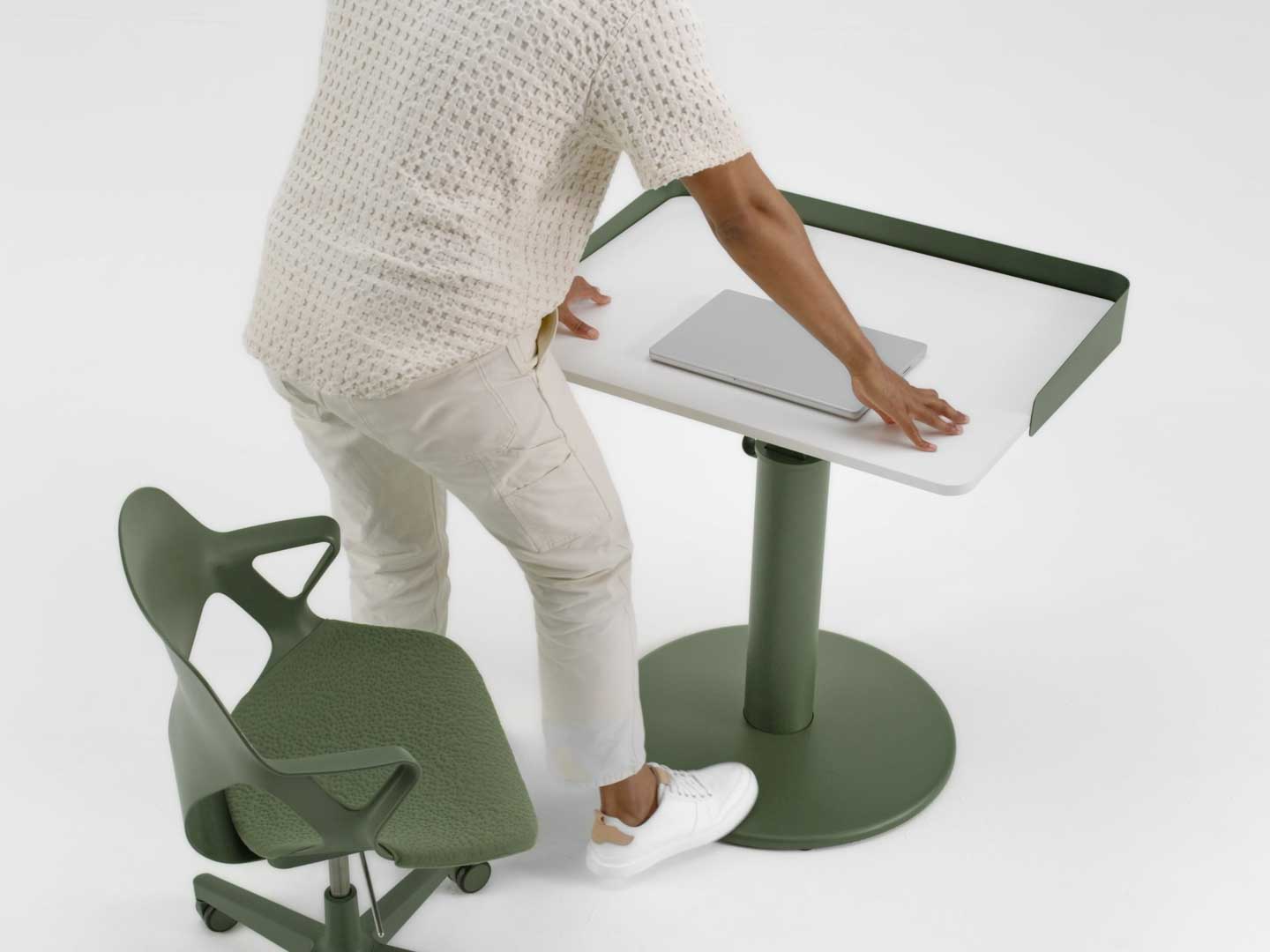 A video of a man standing from a green Zeph chair by Herman Miller and raising the height of a green and white OE1 standing desk by Herman Miller using his foot.