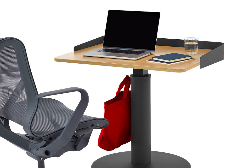 A blue Cosm office chair by Herman Miller, positioned in front of a black and ash OE1 standing desk by Herman Miller, featuring an optional wrap screen.