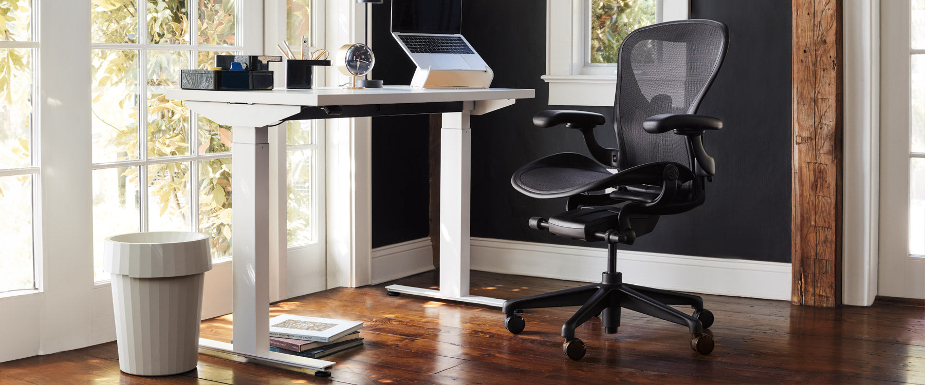 Home office scene containing Nevi sit-stand desk in white with Aeron office chair in onyx black accessorised with Oripura laptop stand and Hay Shade bin in off white