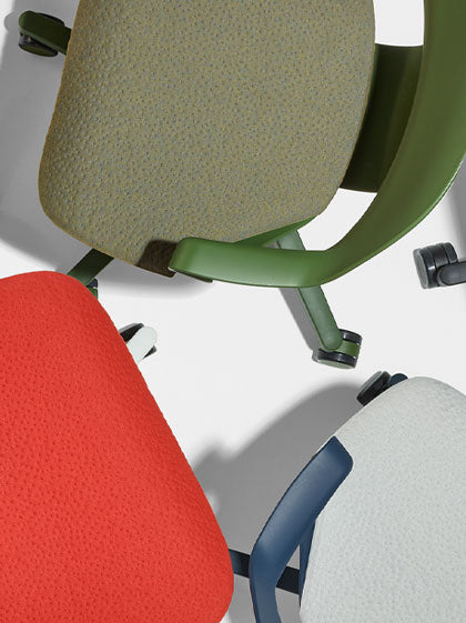 Top view of three Herman Miller Zeph office chairs in green, red and blue, showing the texture of the seat pads.