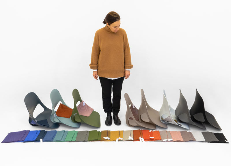 A woman standing beside several Zeph office chair components, with an array of fabric colours laid out in front.