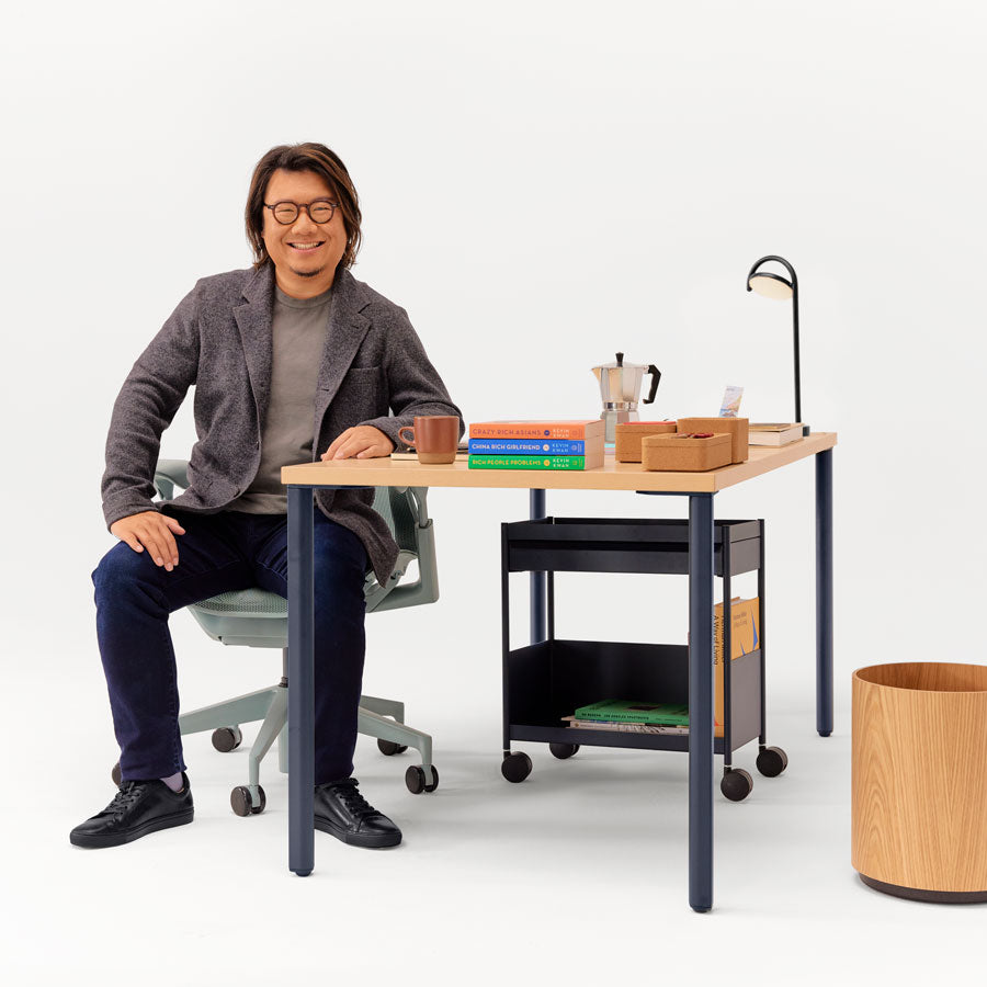 Image of Kevin Kwan sat in low back Glacier Cosm office chair at different angles in front of fixed height OE1 desk in nightfall blue and ash with OE1 storage trolley underneath