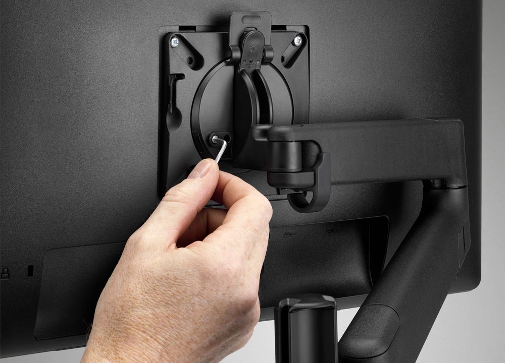 Rear view of a black Lima monitor arm by CBS, featuring a person's hand.