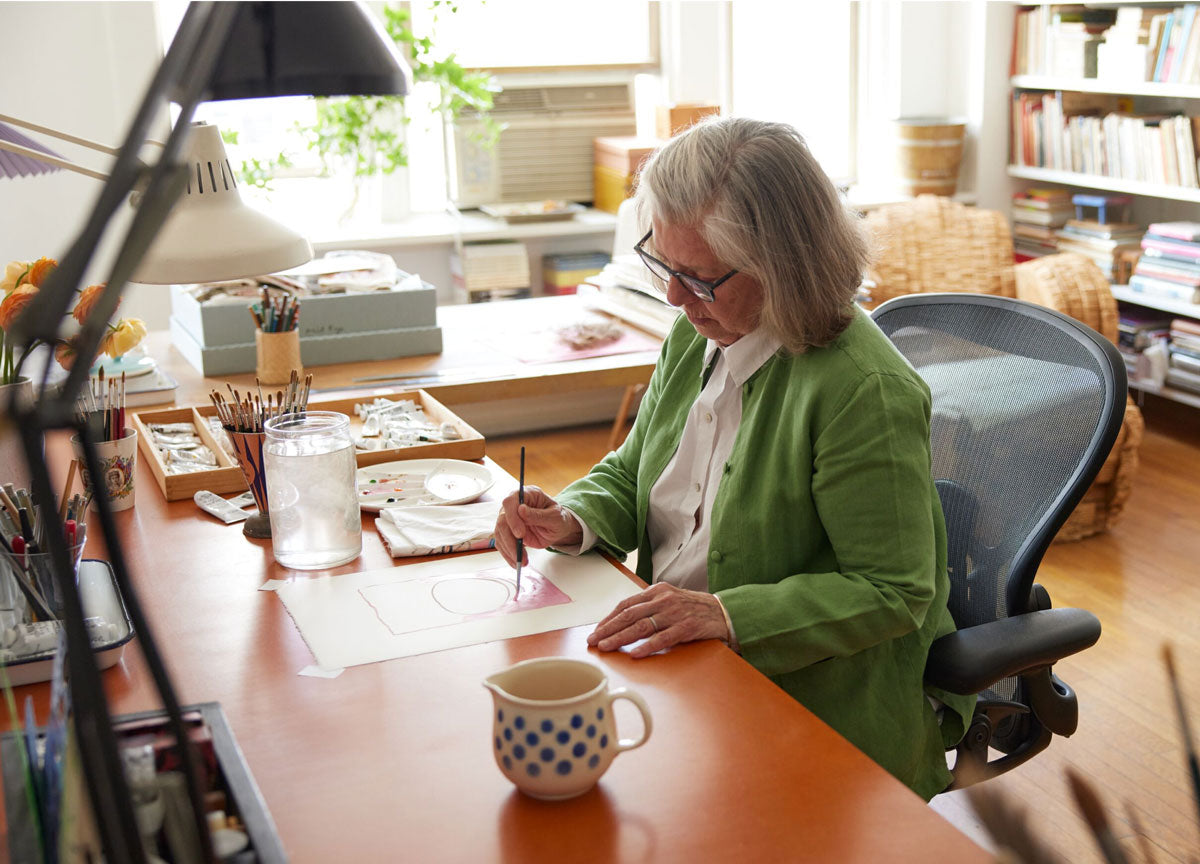 Artist Maira Kalman works on a painting in a bright studio space from her Onyx Herman Miller Aeron.