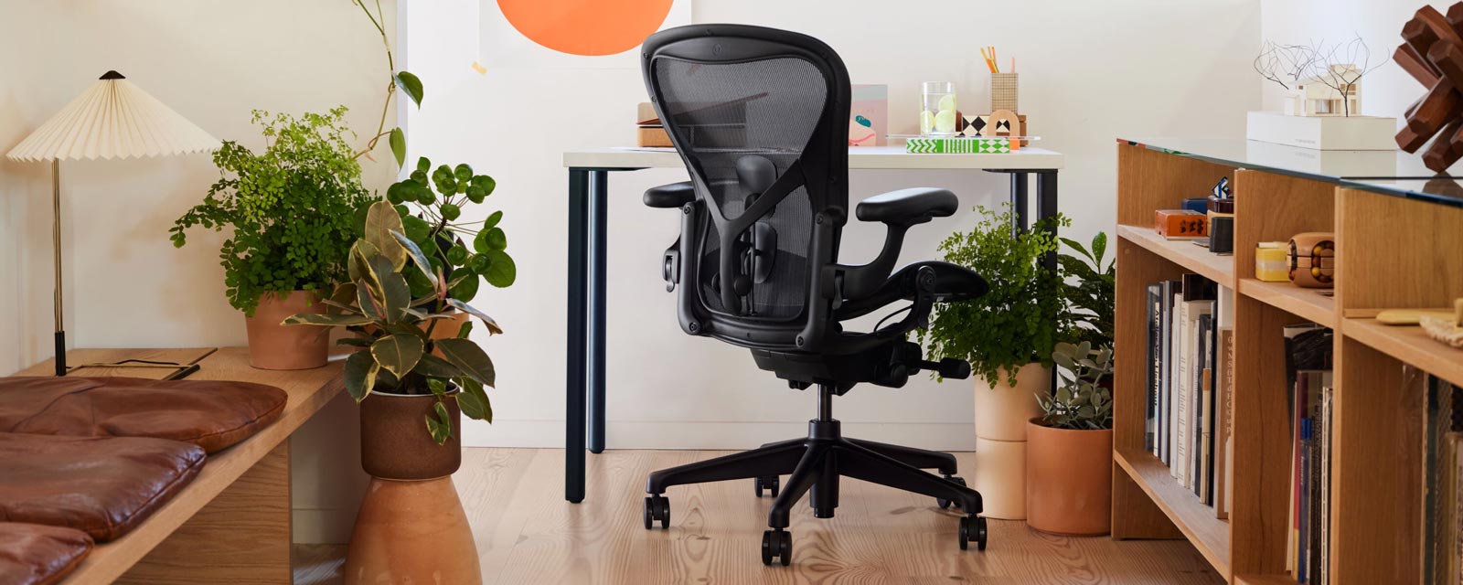 Home office with Iconic Aeron office chair in black in front of small OE1 desk with blue legs and white top, room also has a Hay Matin table lamp
