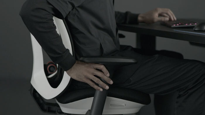 A video of a person sitting in a white and black Vantum gaming chair by Herman Miller, reaching beside the chair to adjust the arms.