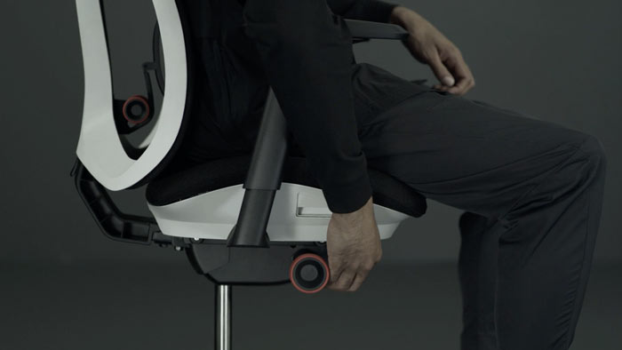 A video of a person sitting in a white and black Vantum gaming chair by Herman Miller, reaching beside the chair to adjust the seat height.