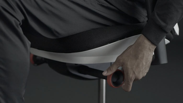 A video of a person sitting in a white and black Vantum gaming chair by Herman Miller, reaching beside the chair to adjust the tilt limiter.