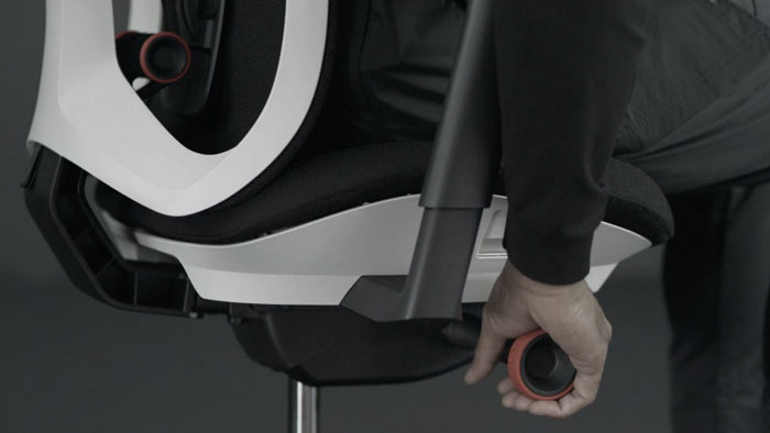 A video of a person sitting in a white and black Vantum gaming chair by Herman Miller, reaching beside the chair to adjust the tilt tension.