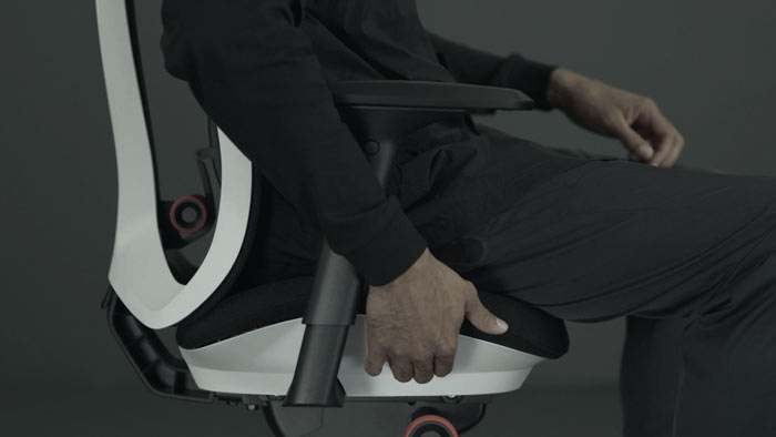 A video of a person sitting in a white and black Vantum gaming chair by Herman Miller, reaching beside the chair to adjust the seat depth.