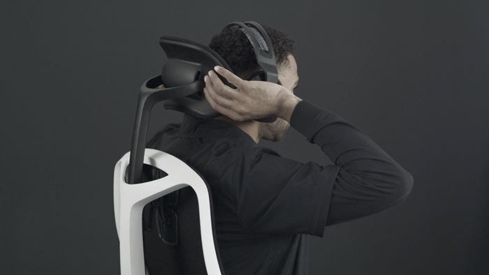 A video of a person sitting in a white and black Vantum gaming chair by Herman Miller, reaching behind the chair to adjust the headrest.