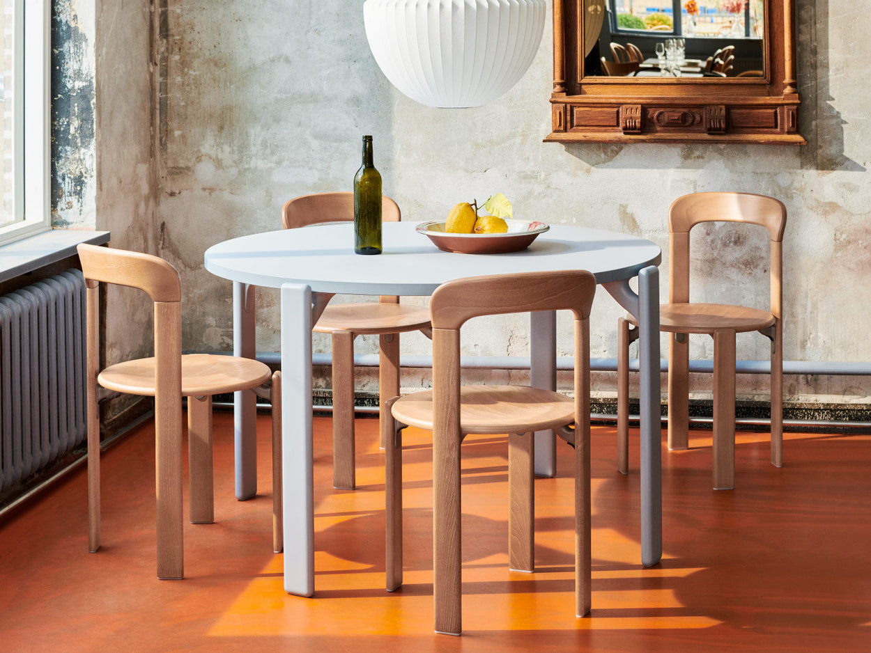 Four beech Rey chairs by HAY, positioned around a slate blue Rey dining table. Set in a home environment, with a Nelson pendant above the table and a fruit bowl and a bottle of wine on the tabletop.