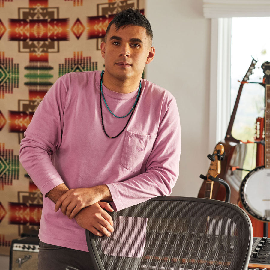 Photo of Rostam, muscian, producer and composer, stood leaning on Aeron office chair in graphite with musical instruments in the background