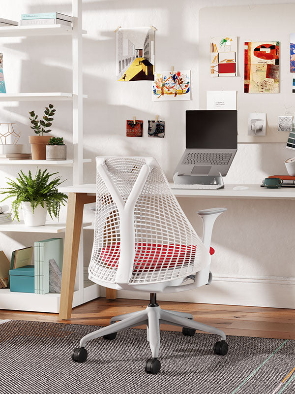 Sayl home office chair with white frame, gray base and red upholstered seat in home office setting, with shelving and plants and laptop on an white oripura stand.
