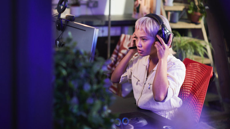 A video of a woman sitting in a red and black Sayl gaming chair by Herman Miller, putting on headphones and playing a computer game.