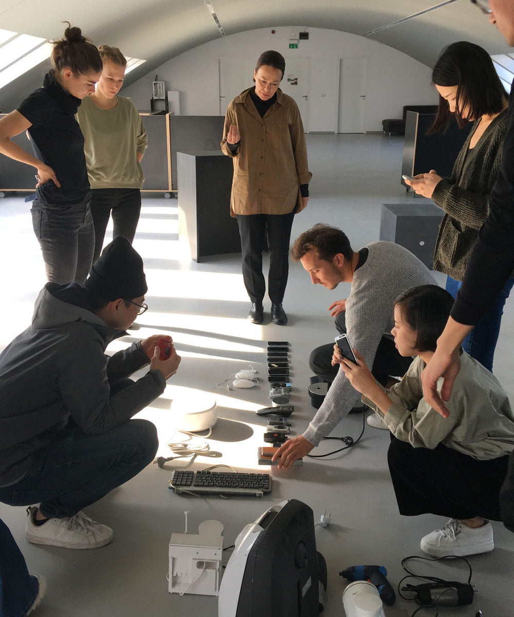 Photograph of Studio 7.5 designers looking a various small electonics laid on on the floor
